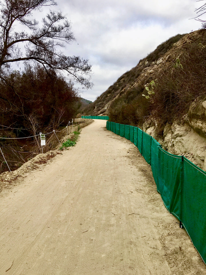 Green weather barrier on an access road next to a hill