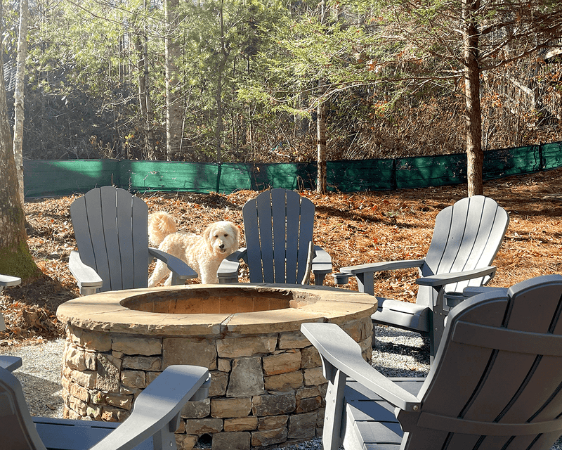 Load image into Gallery viewer, Dog by a fire pit and chairs in a backyard with green weather barrier in background
